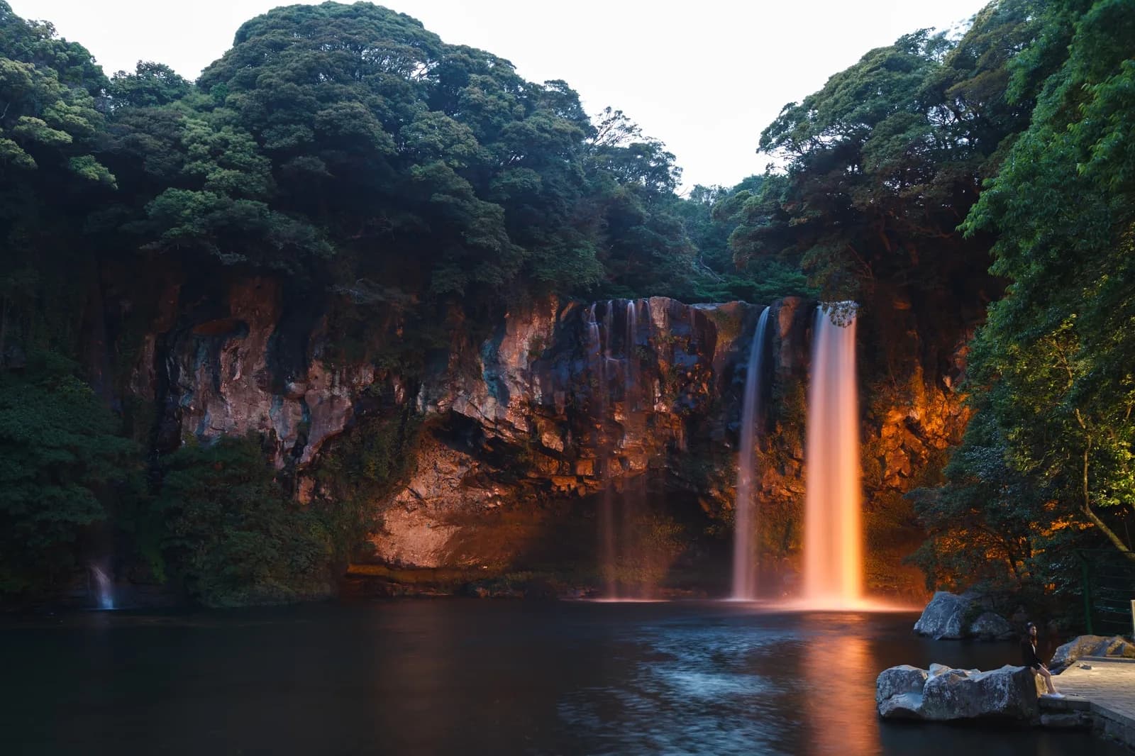 Cheonjiyeon Falls and its pool lit orange in the evening